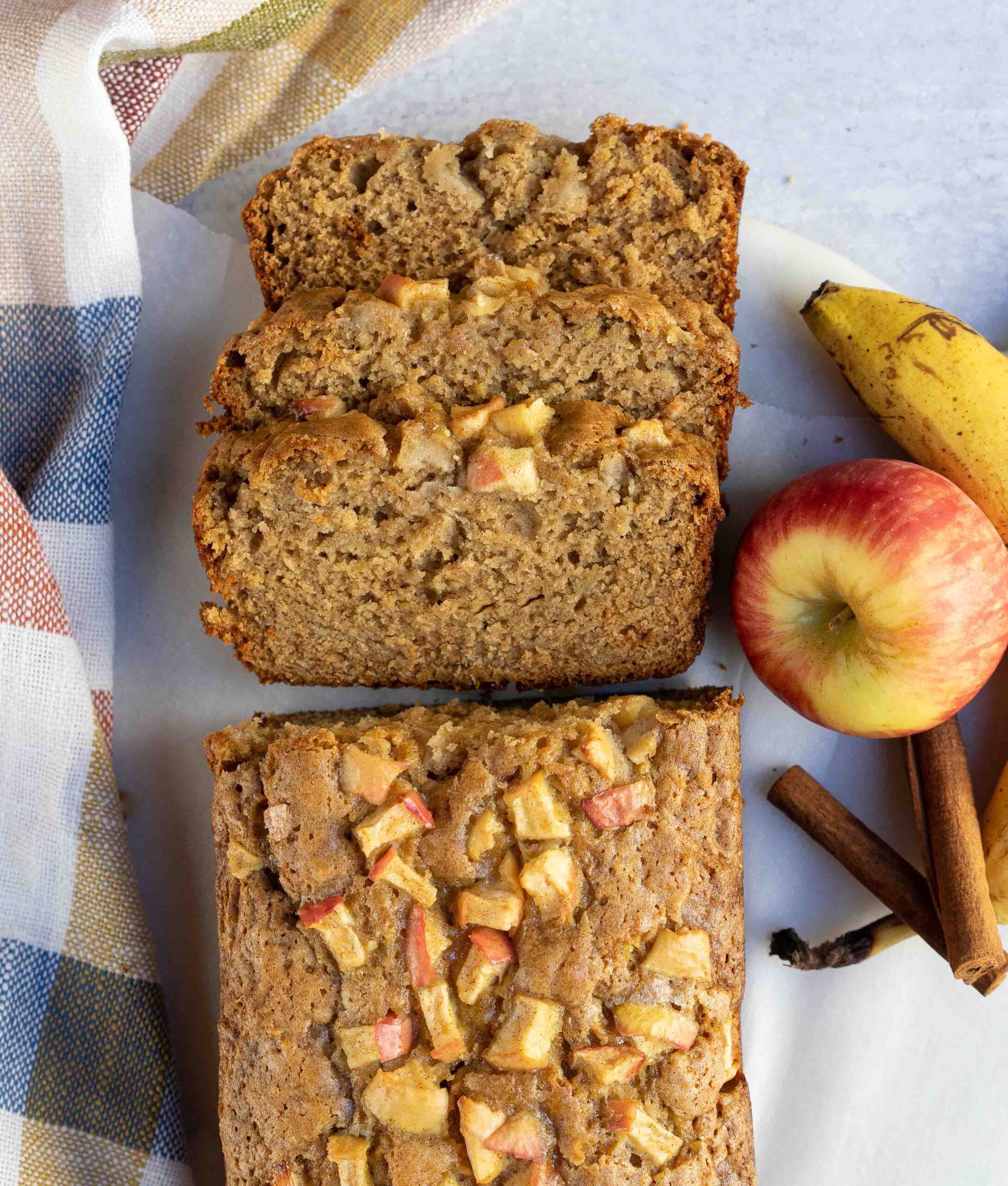 banana apple bread sliced with apple and banana next to it.