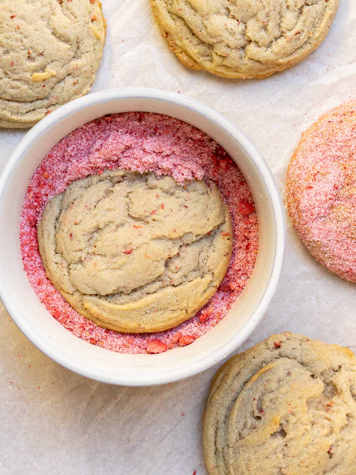 strawberry sugar cookie in a bowl being coated with strawberry sugar.