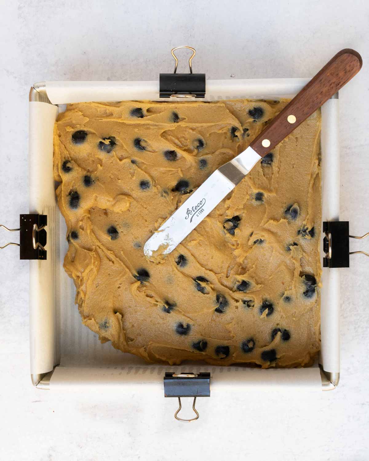 blueberry blondie batter being spread in baking pan with spatula.