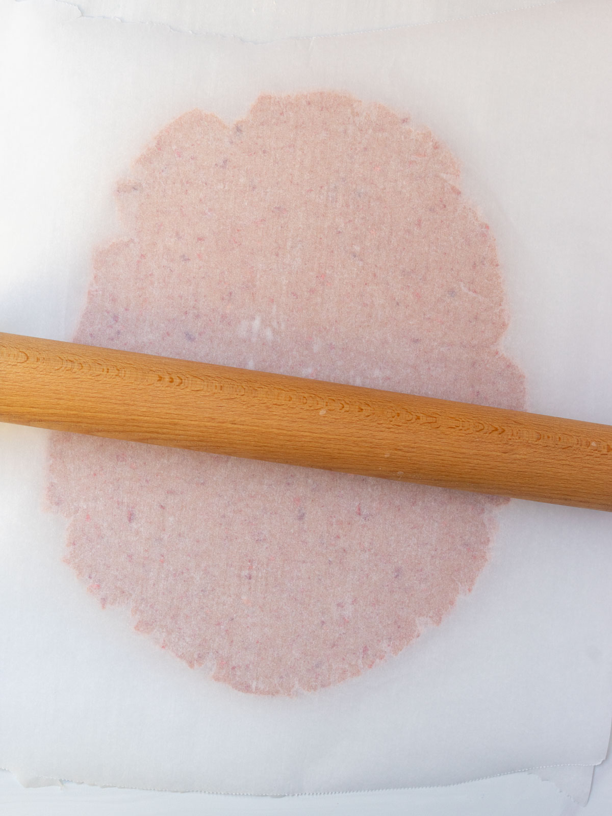 strawberry sugar cookie dough being rolled out between two pieces of parchment paper.